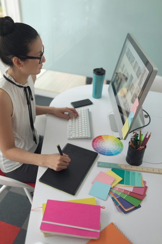 High angle view of Asian female graphic designer using graphic tablet at desk in a modern office