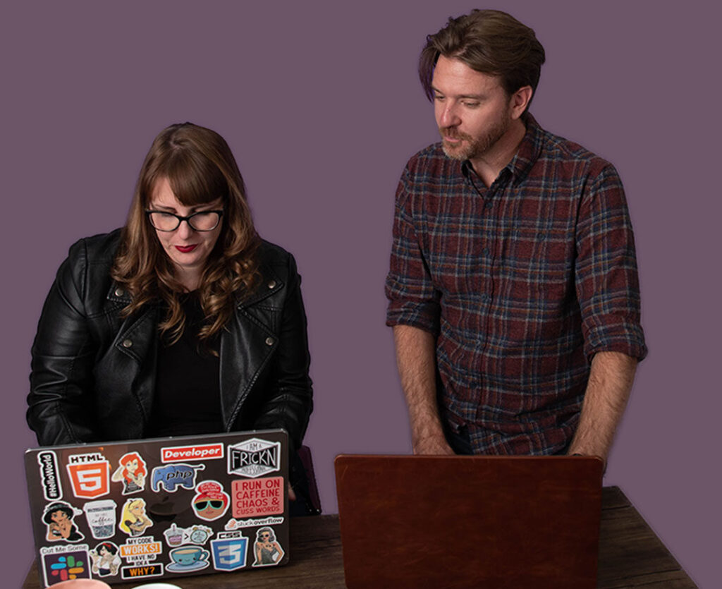 Two people working together on sticker-covered laptop