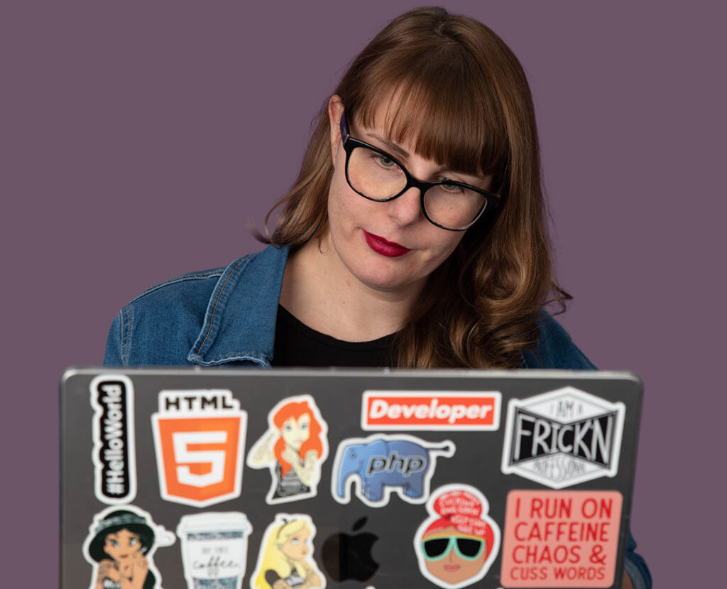 Woman with glasses working on sticker-covered laptop