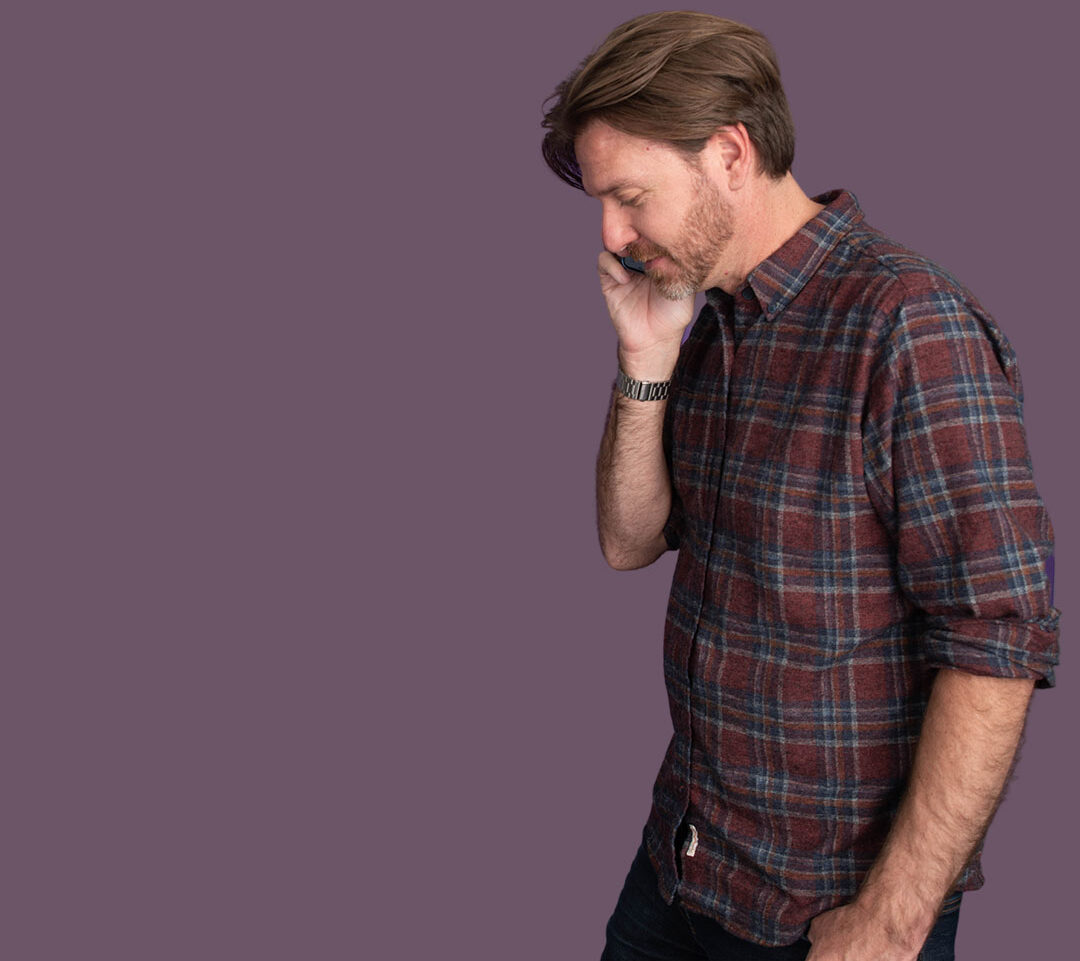 Man in plaid shirt looking down with hand on face.