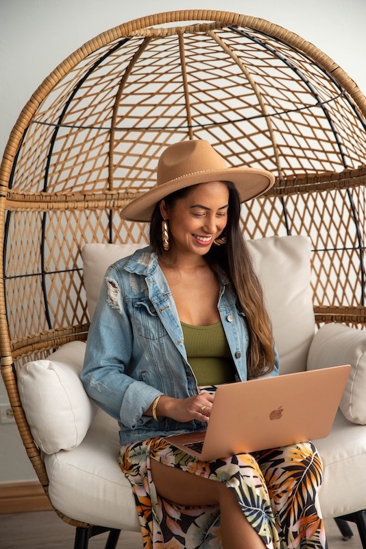 Woman in hat using laptop in wicker chair